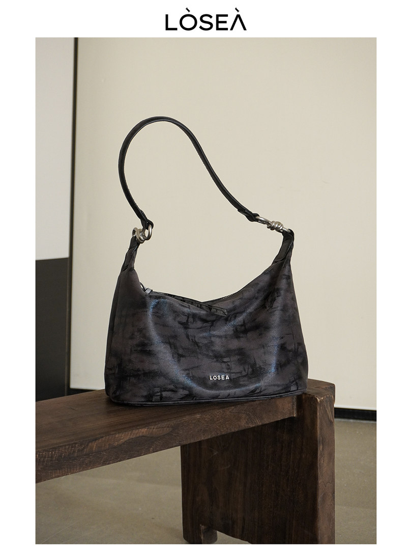 Black shoulder handbag with a single strap on a wooden bench