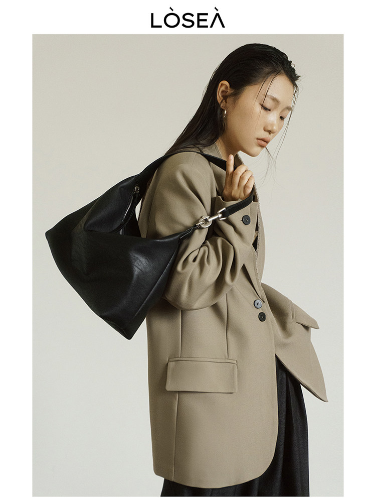 Model wearing a black leather shoulder bag with a beige blazer coat