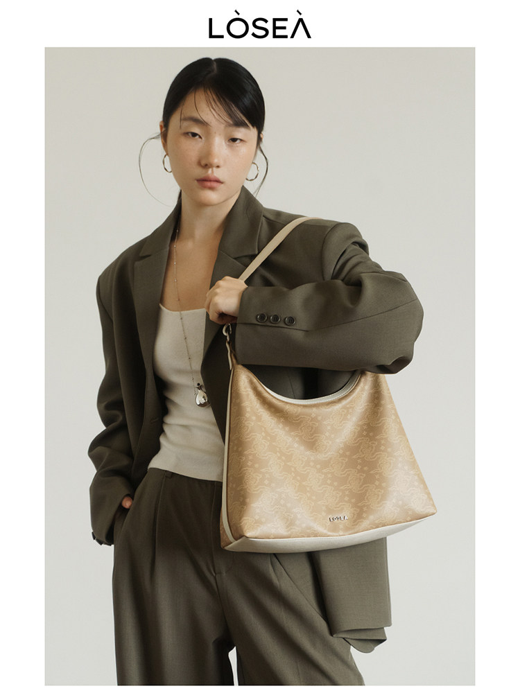 Beige patterned shoulder handbag worn by a model in an olive suit