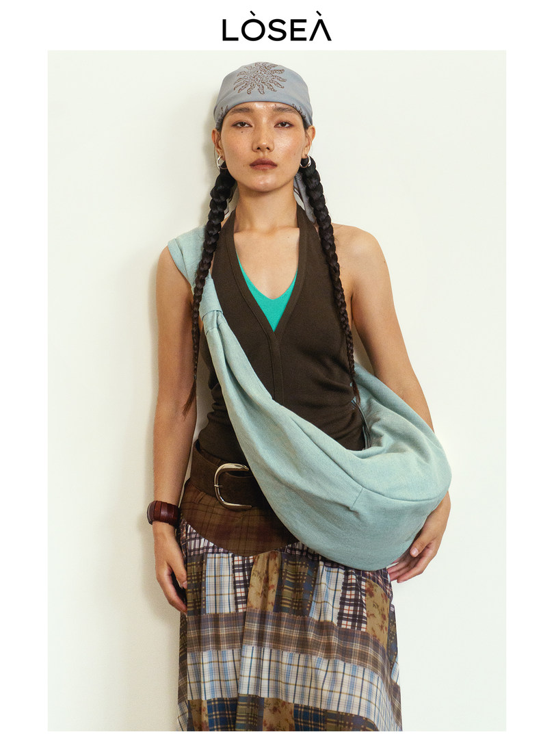 Fashion model wearing a layered streetwear outfit with a headscarf, sleeveless top, and plaid skirt