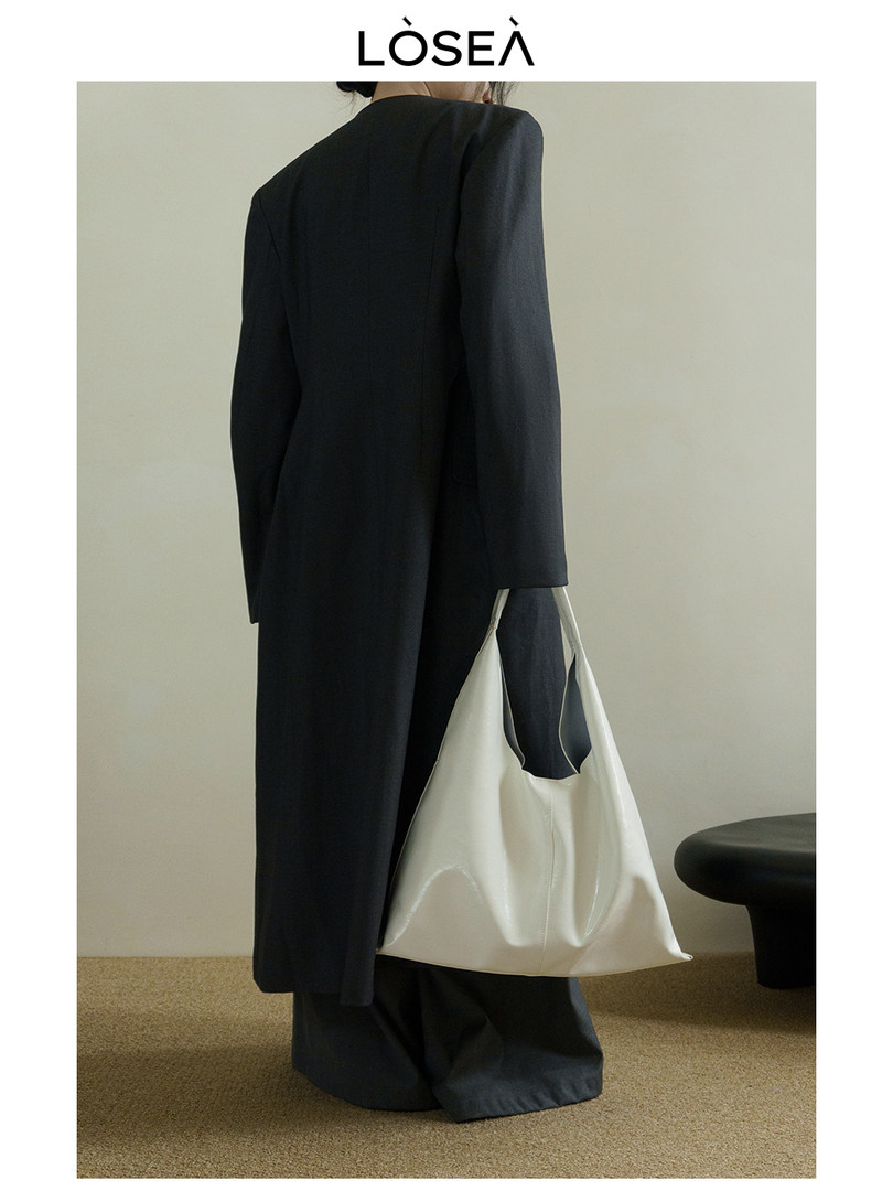 Model wearing a long black coat and carrying a white tote bag
