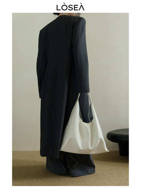 Model wearing a long black coat and carrying a white tote bag