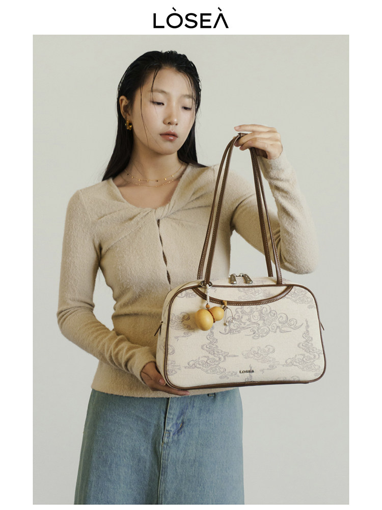 Model holding a cream patterned handbag with brown straps