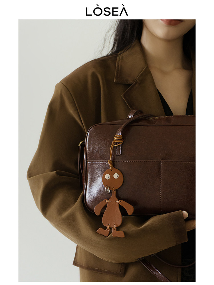 Brown leather handbag held by a model with a small dangling charm