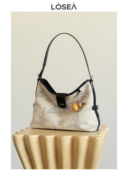 Patterned beige shoulder handbag with black trim and pendant charm on display
