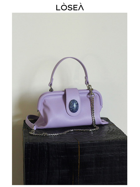 Lavender handbag with chain strap and top handle on a pedestal