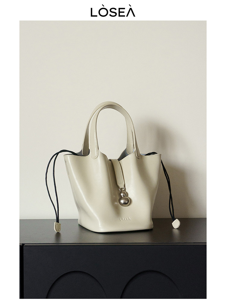 Cream tote handbag with drawstring details on a dark surface