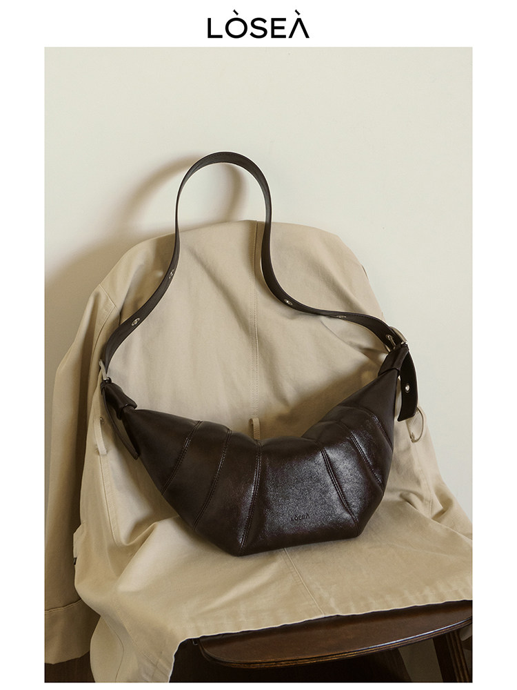 Dark brown leather crescent shoulder bag displayed on a chair