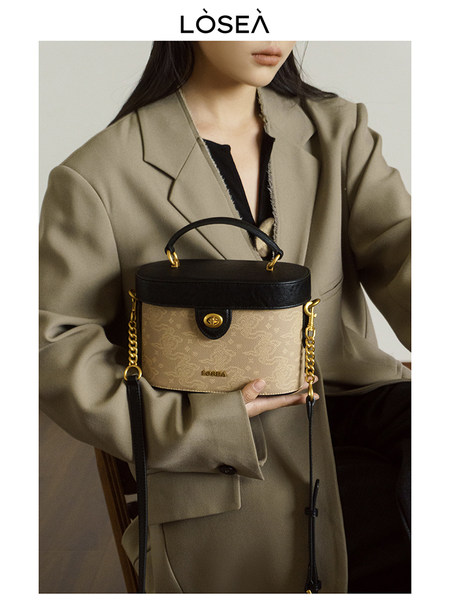 Model holding a beige and black structured handbag with gold chain details