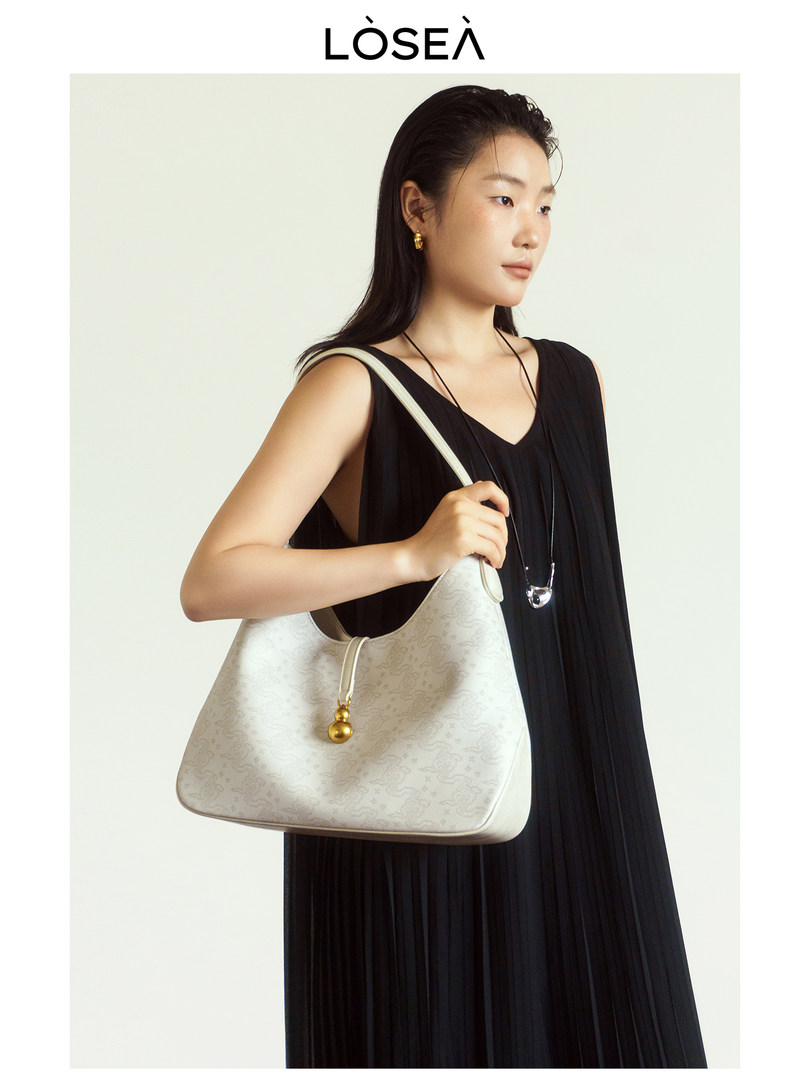 Model wearing a black dress and holding a light beige luxury handbag