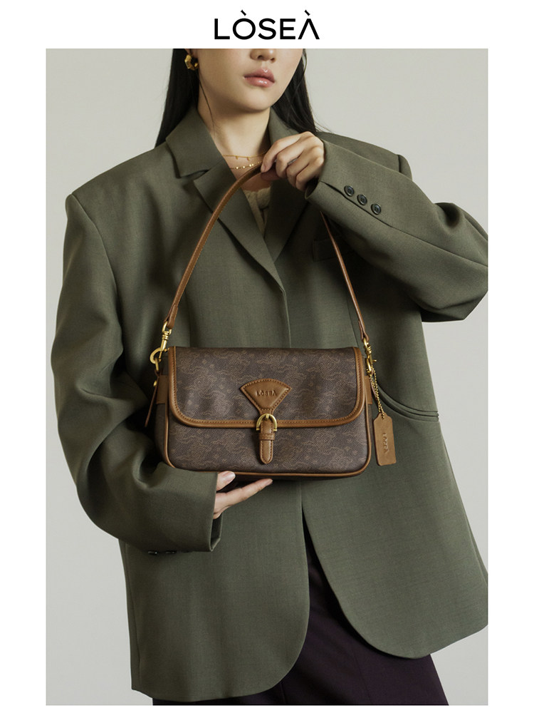 Brown monogram shoulder handbag held by a model wearing an oversized blazer