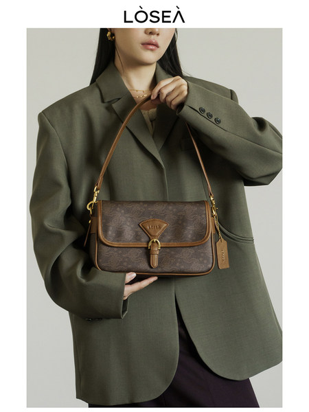 Brown monogram shoulder handbag held by a model wearing an oversized blazer