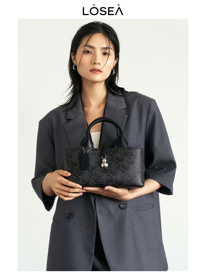 Black patterned handbag held by a model in a gray blazer