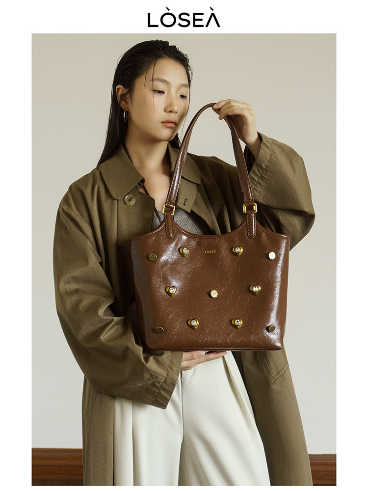 Brown leather tote handbag with gold stud details held by a model