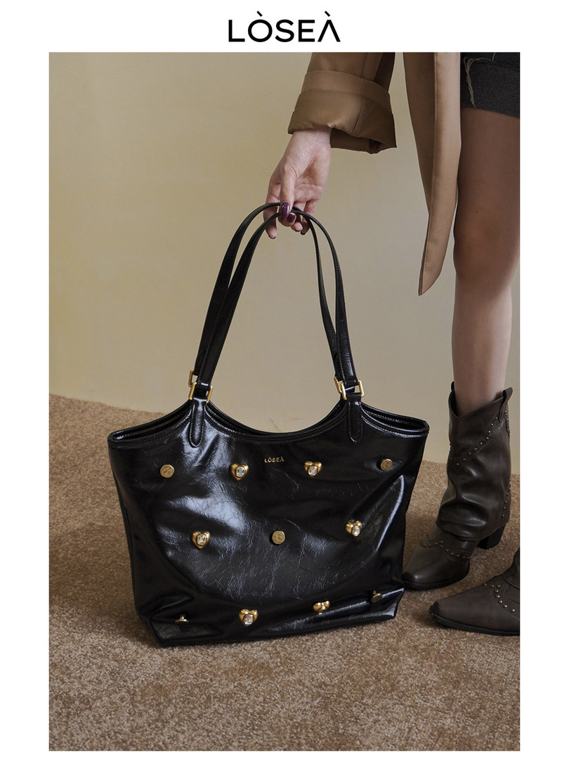 Black studded leather tote handbag being held by a model