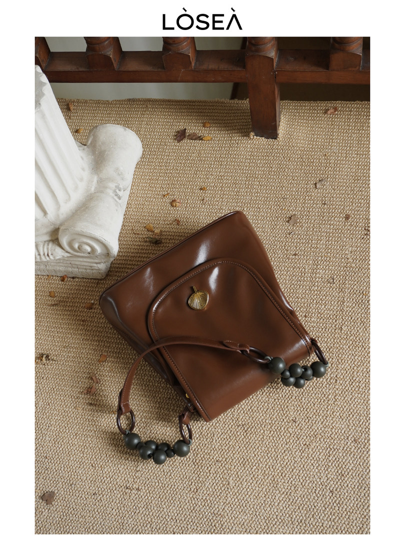 Brown leather handbag with beaded strap on woven surface
