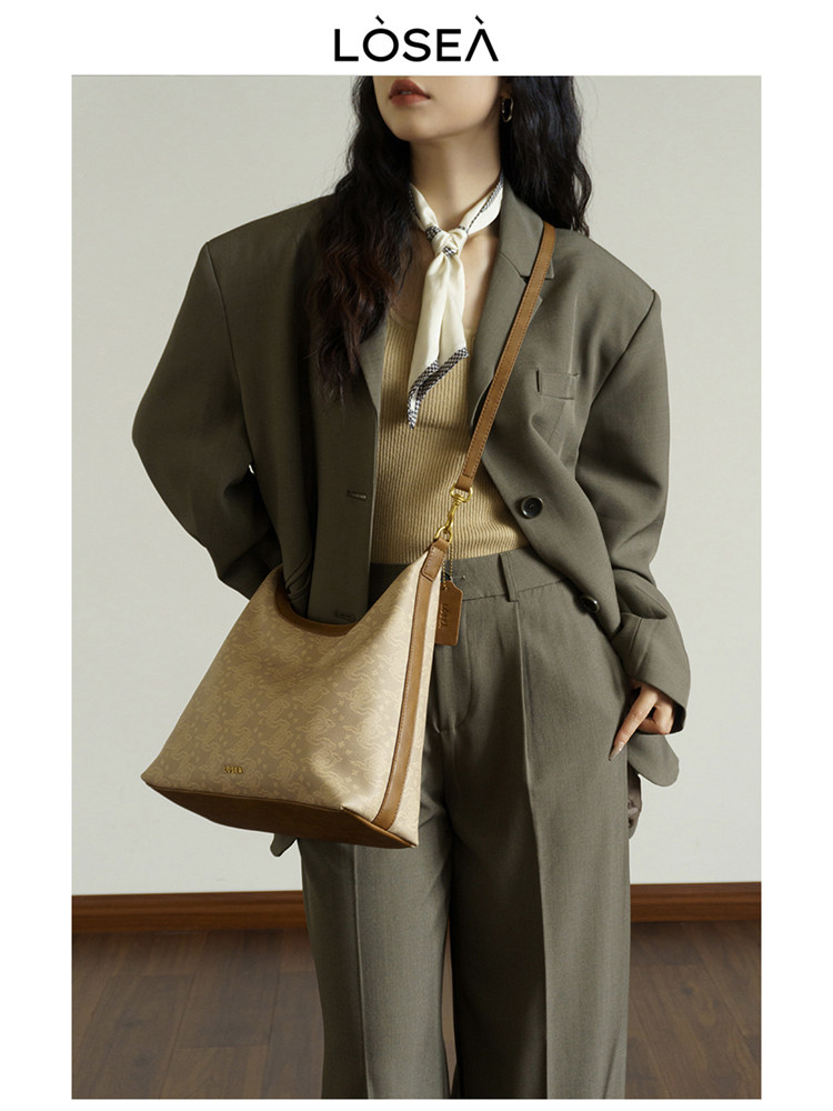 Model wearing an olive suit with a beige tote bag and scarf