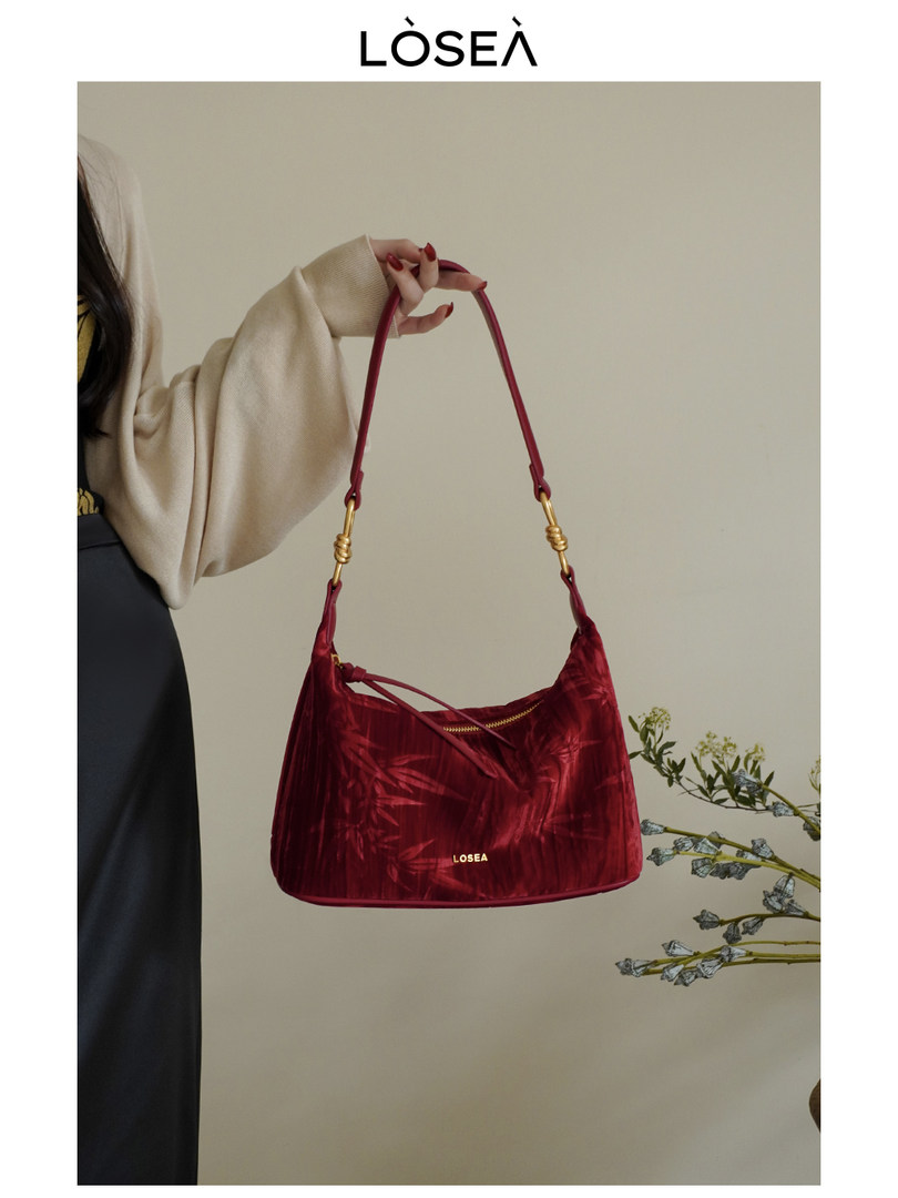 Red velvet shoulder handbag held by a model