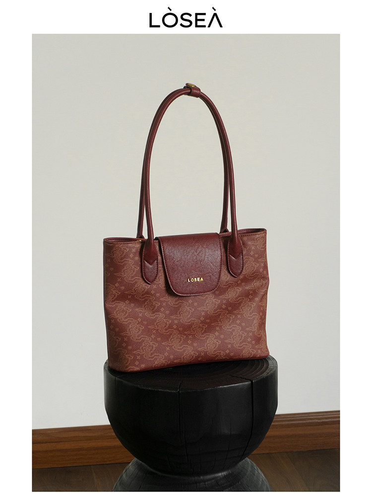 Burgundy tote handbag with long handles on a display stand
