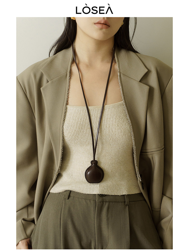 Model wearing a beige blazer over a ribbed tank top with a long pendant necklace