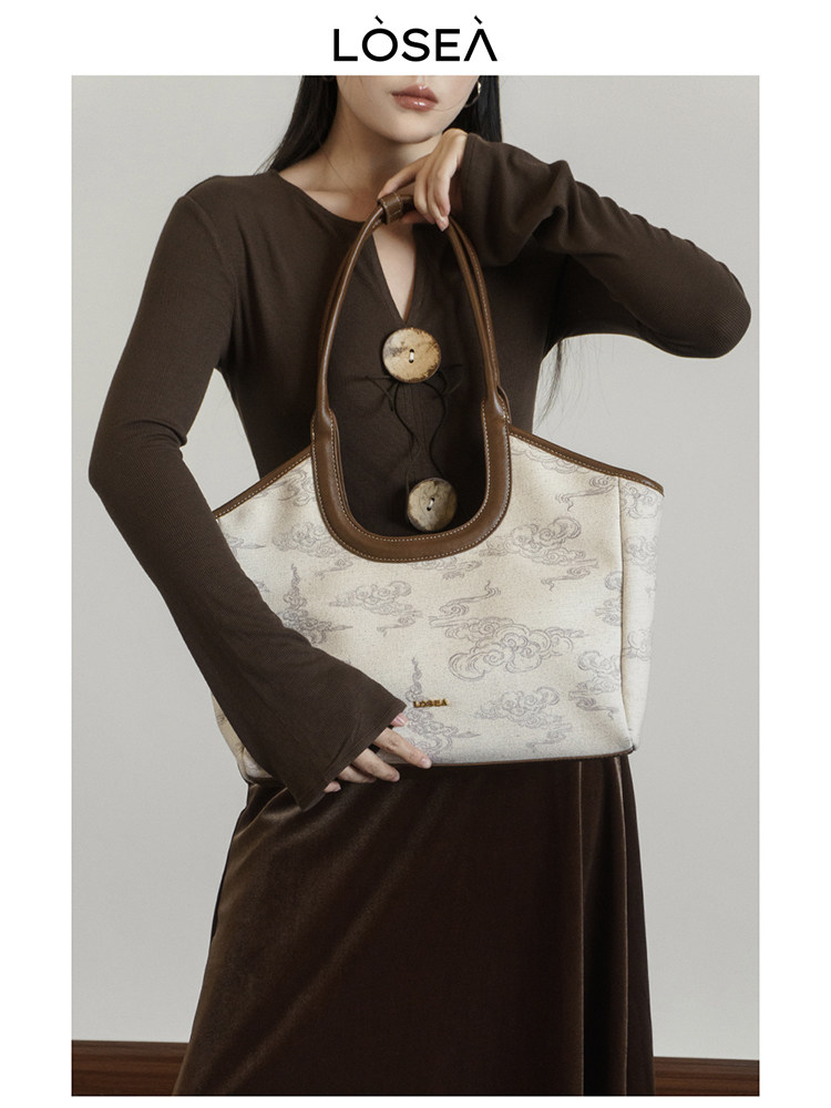 Model holding a cream patterned tote handbag with brown handles