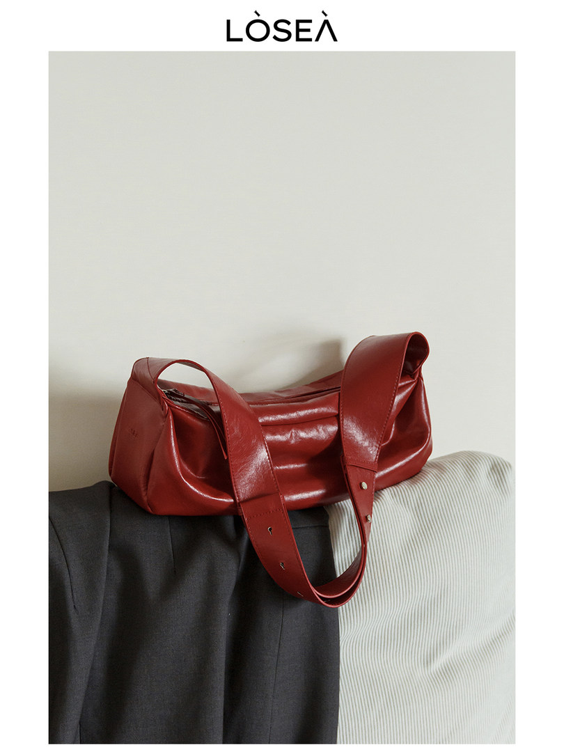 Red leather handbag with long strap on a neutral background