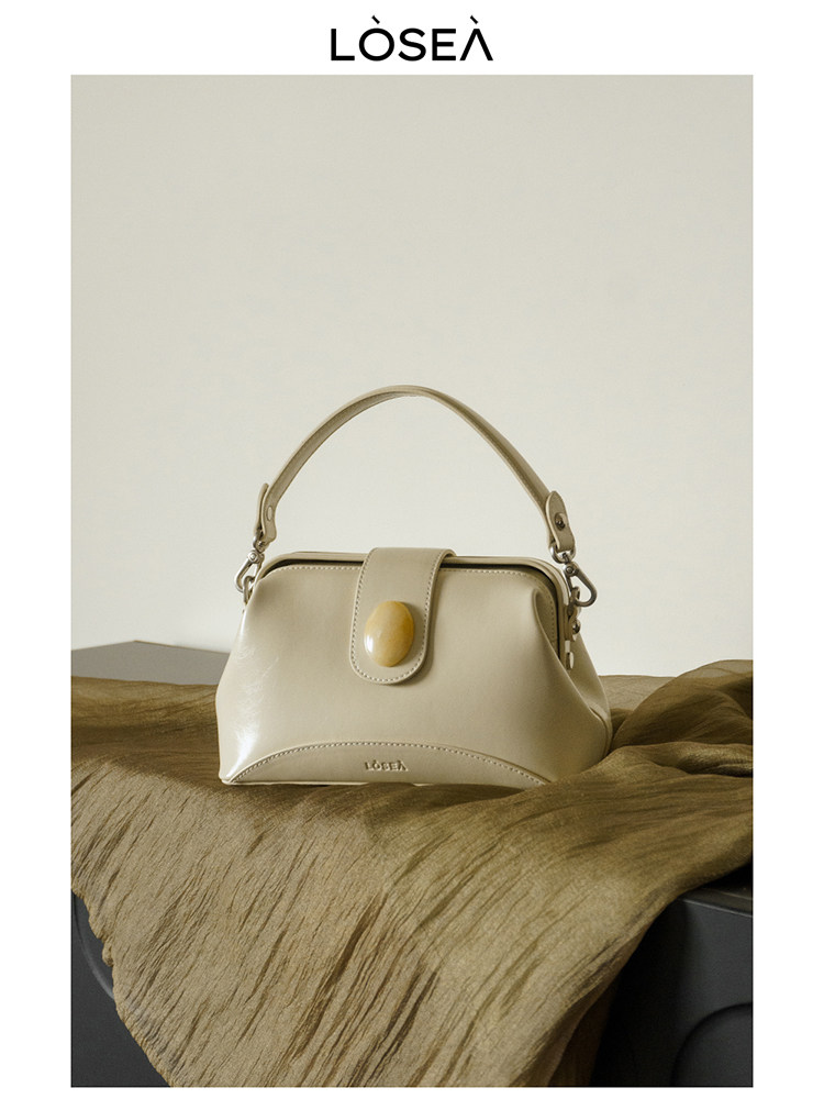 Beige leather handbag with a top handle and round clasp detail