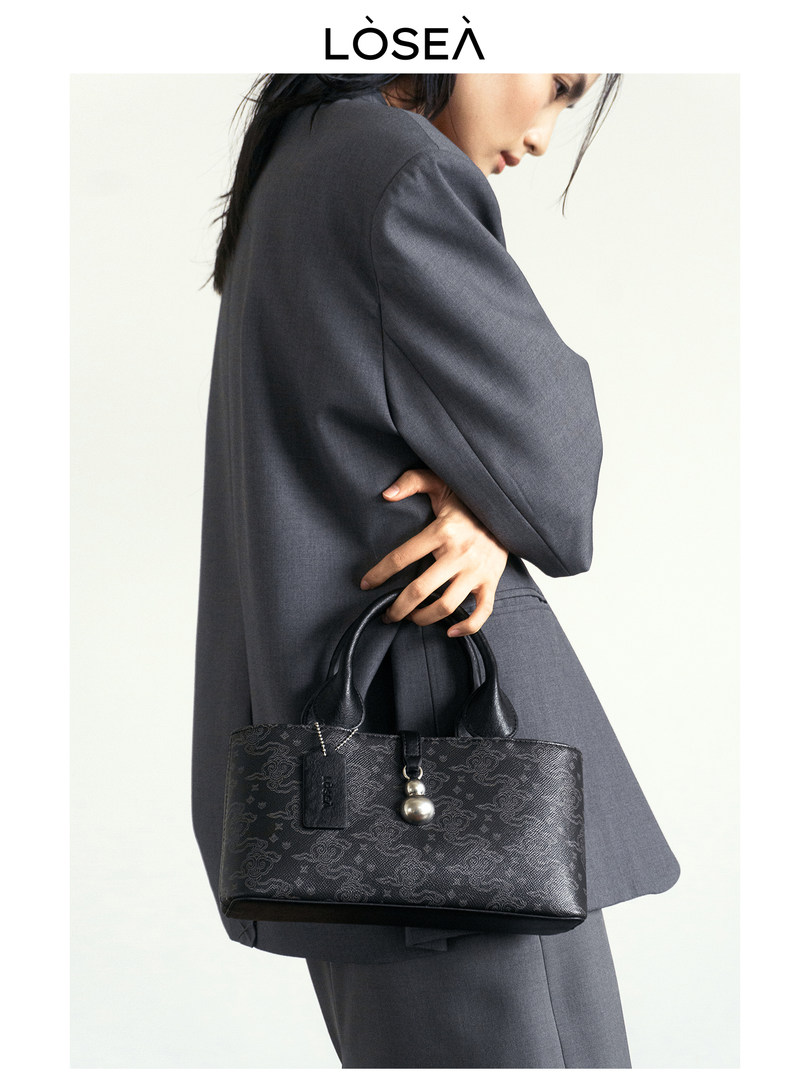 Model carrying a black patterned handbag with decorative charm