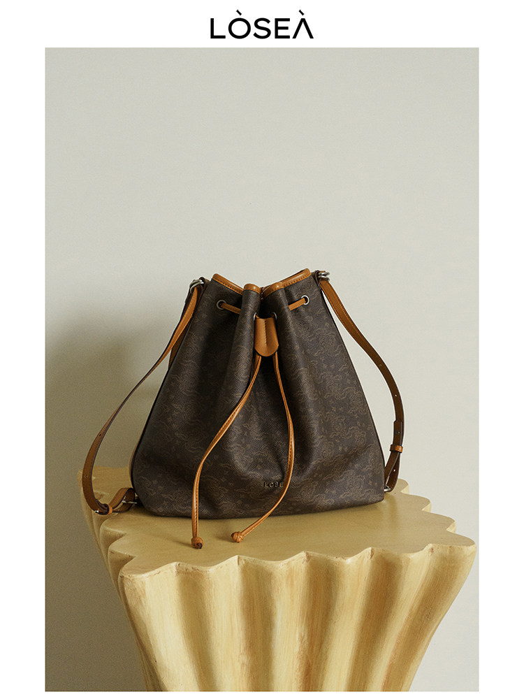 Brown drawstring bucket handbag on a pedestal with brand logo above