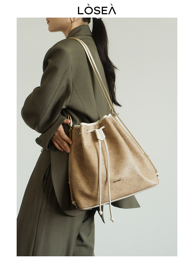 Beige drawstring shoulder bag worn by a model in an olive coat