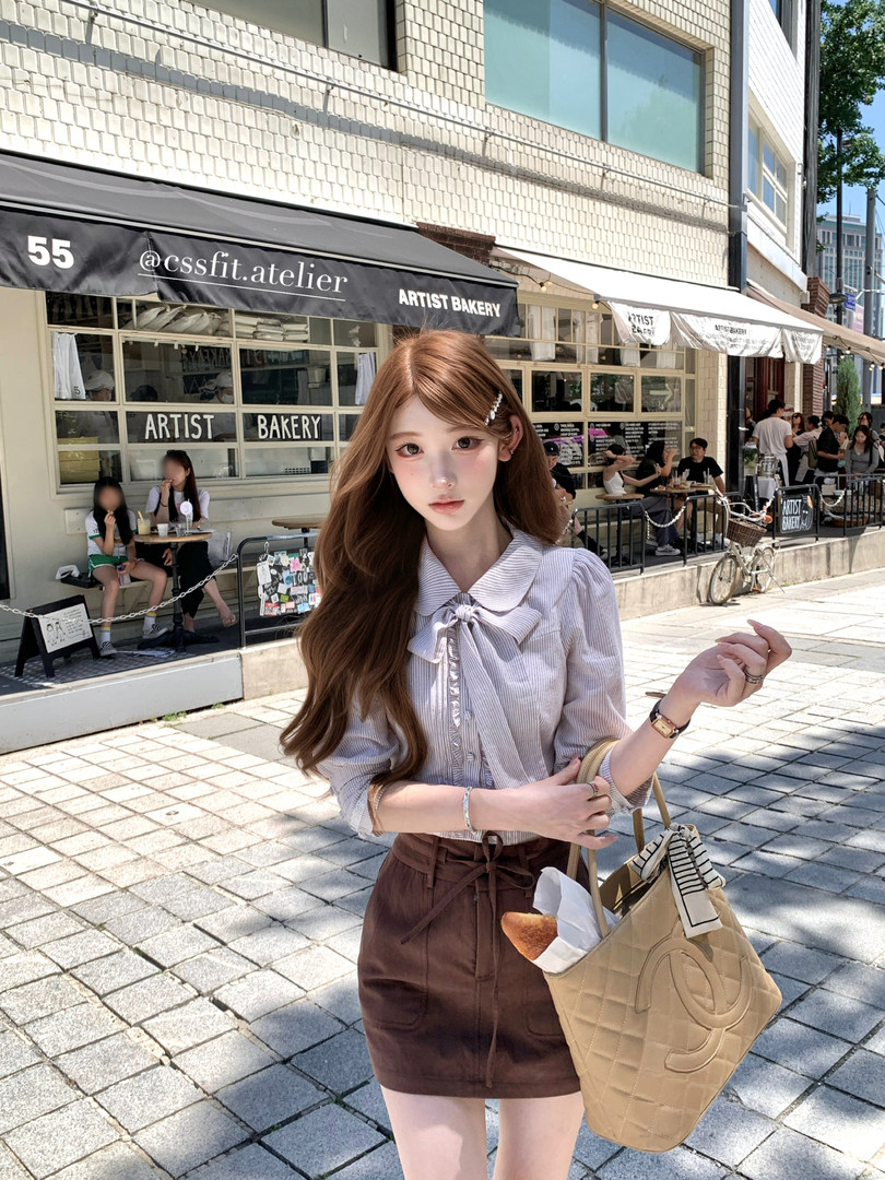 Woman wearing a light striped blouse and brown high-waist mini skirt with a beige tote bag on a city street