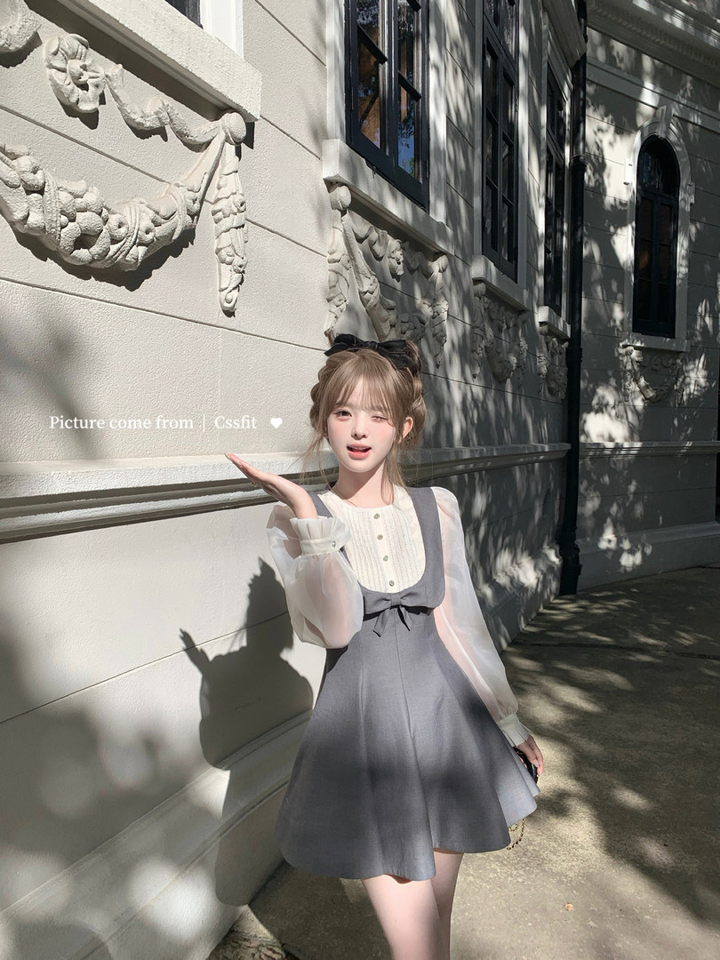 Woman wearing a gray pinafore dress with sheer long sleeves outdoors
