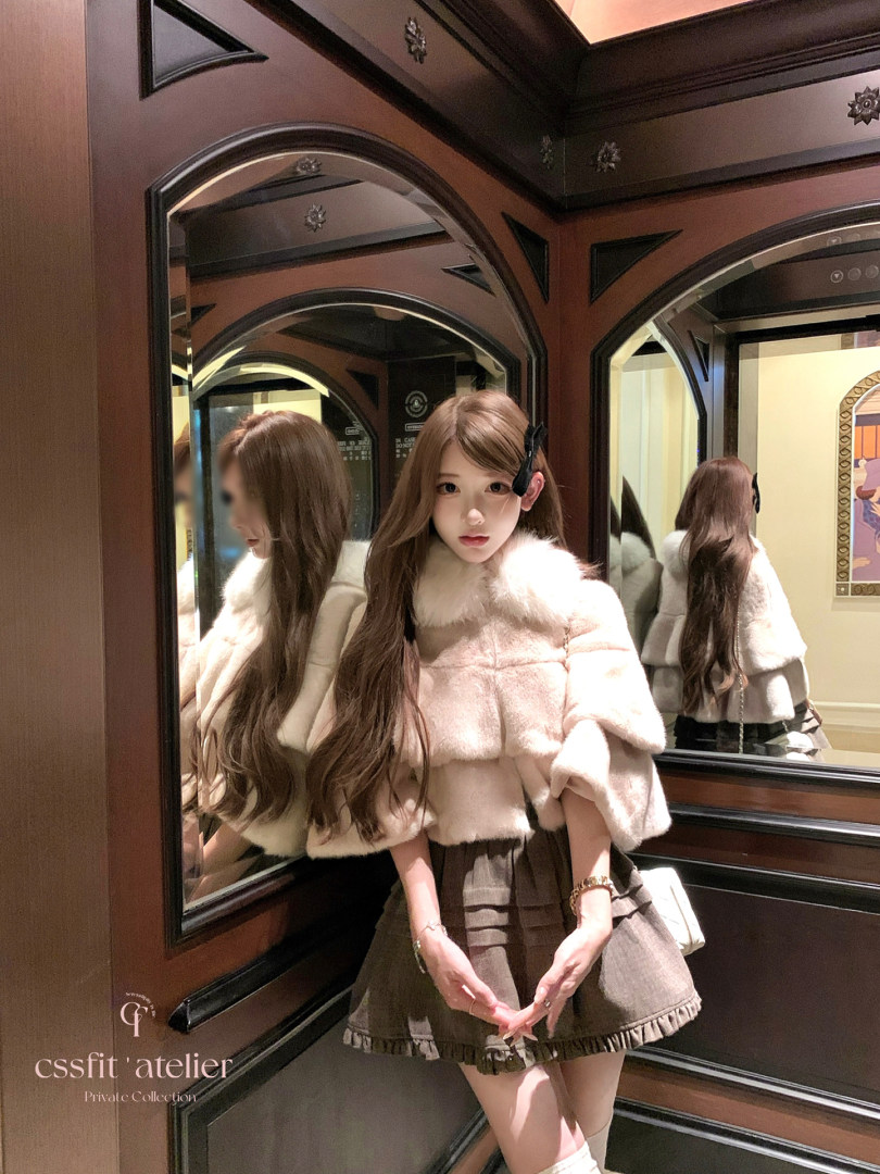 Woman wearing a pink fur-trimmed top and brown ruffled skirt in a mirror elevator