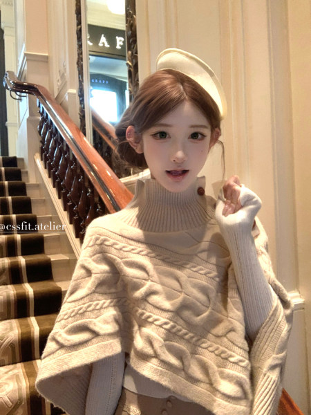 Woman wearing a beige cable-knit turtleneck poncho sweater