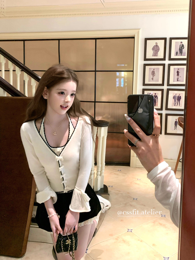 Woman wearing a white-and-black cardigan top in a mirror selfie