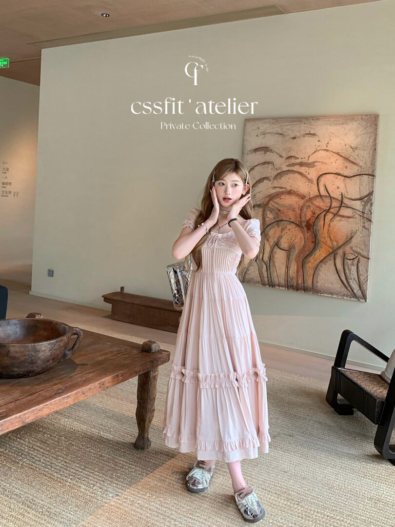 Woman wearing a light pink ruffled midi dress and metallic shoes indoors