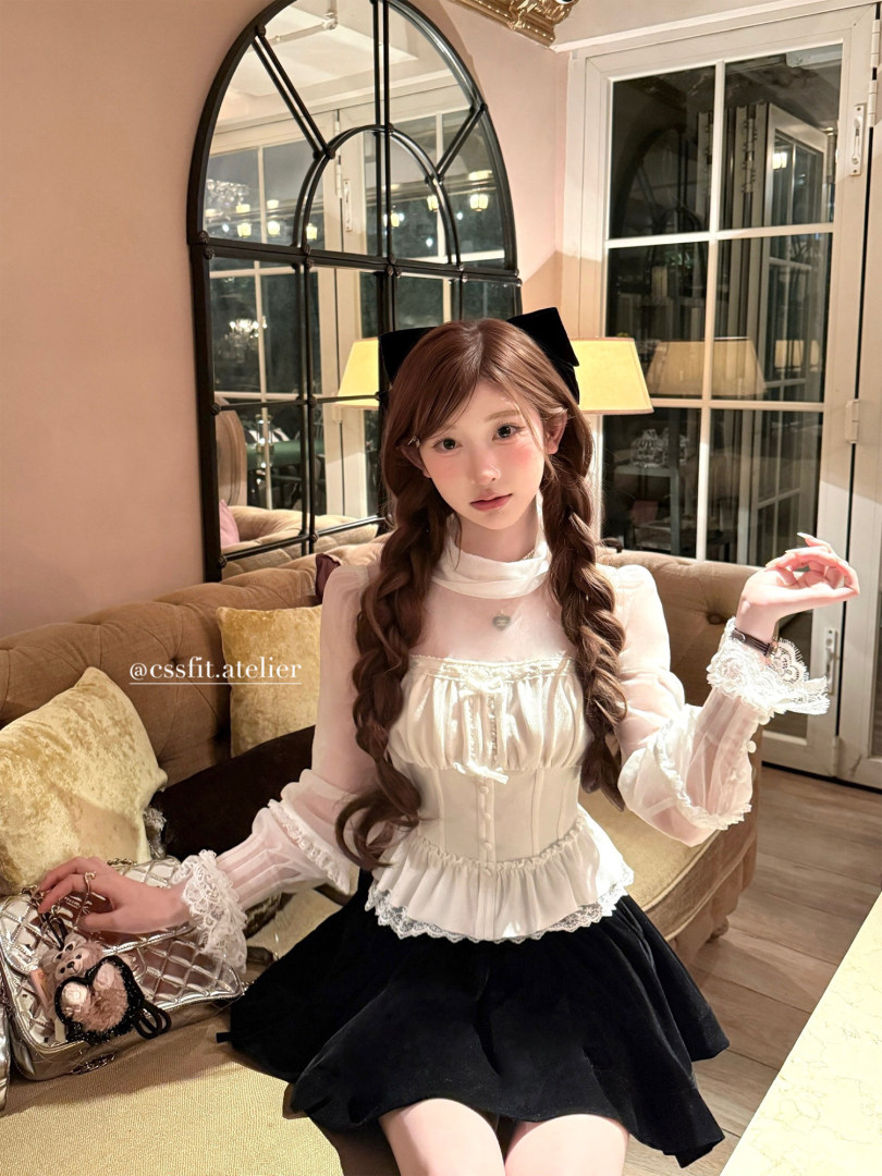 Woman wearing a white lace-trim blouse with a black skirt indoors