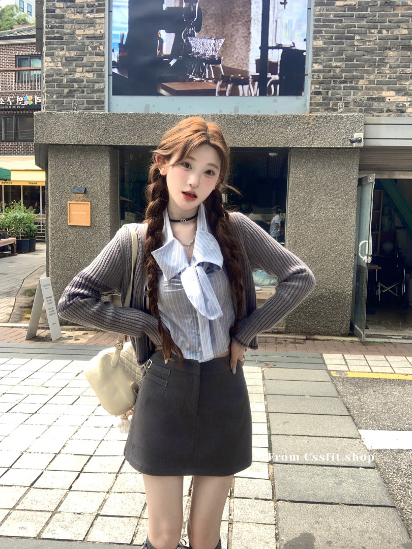 Woman wearing a gray ribbed cardigan over a striped blouse with a black mini skirt outdoors