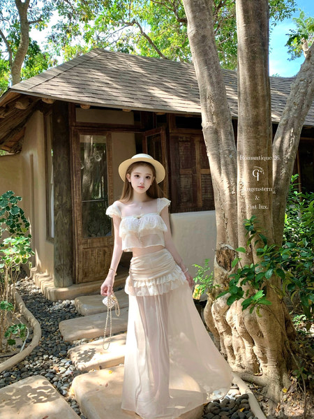 Woman wearing a white sheer two-piece vacation outfit with hat outdoors