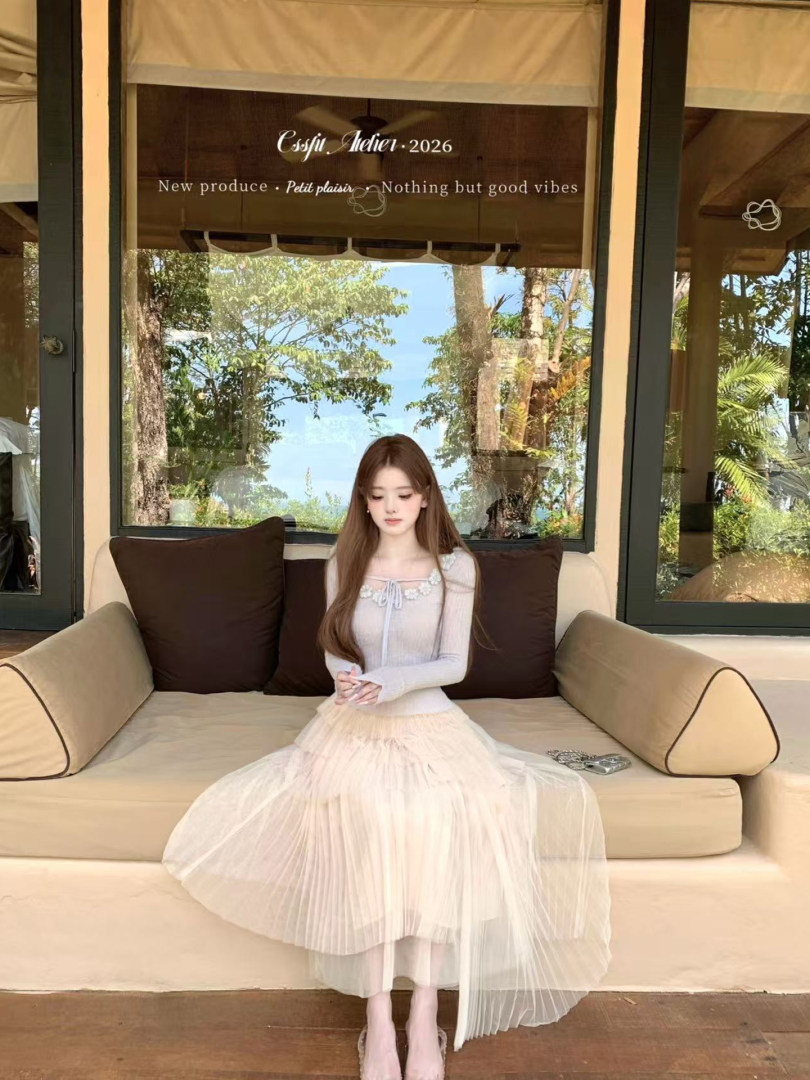 Woman wearing a light pastel long-sleeve top with a layered tulle skirt while seated on a sofa