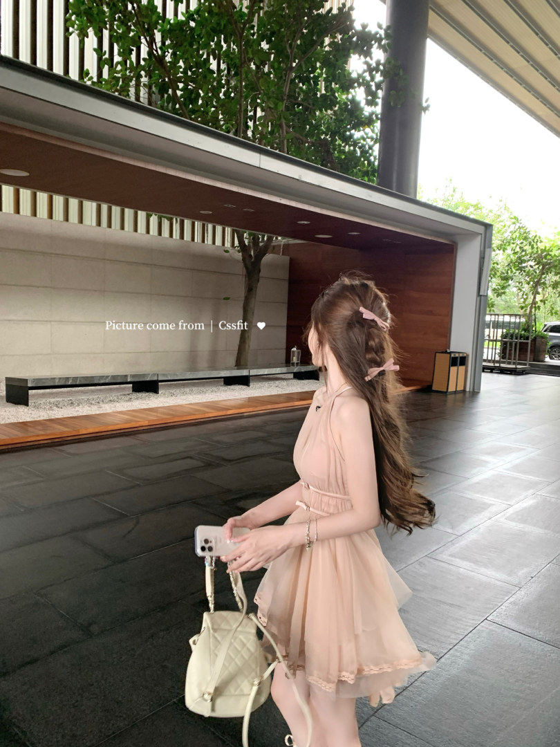 Woman wearing a light pink sleeveless layered dress and holding a quilted cream handbag