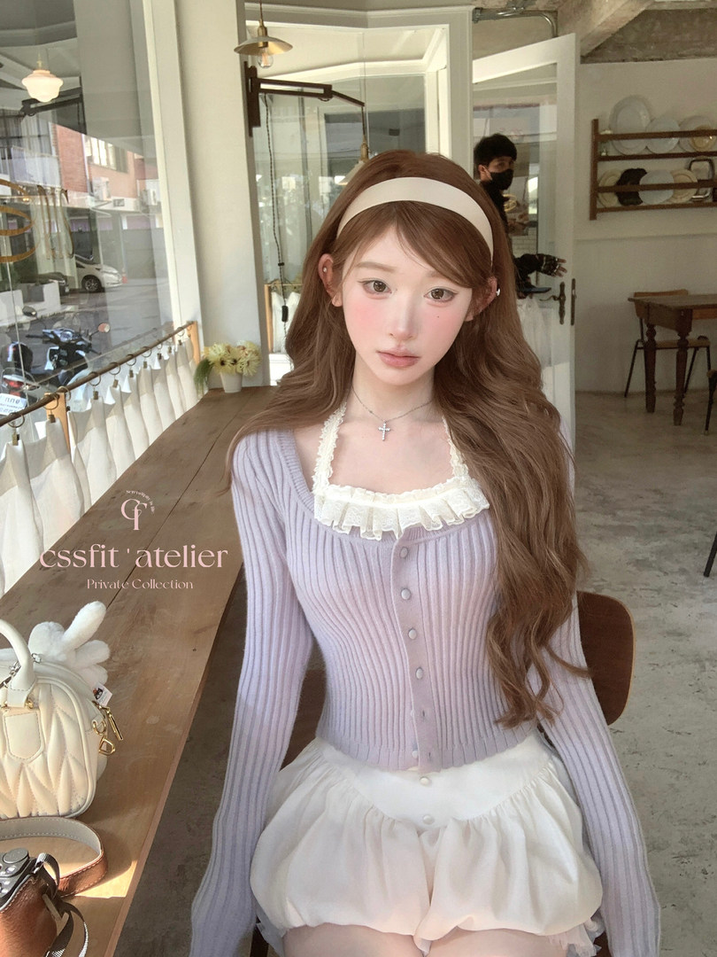 Woman wearing a lilac ribbed cardigan and white ruffled shorts in a boutique