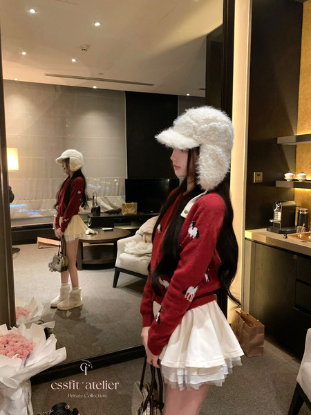 Woman wearing a red patterned sweater, white layered skirt, and fluffy winter hat