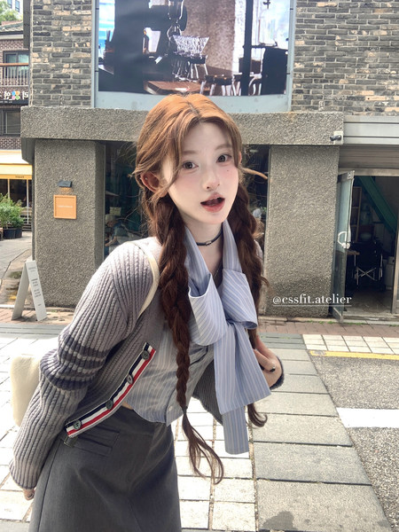 Young woman wearing a gray cardigan over a striped shirt with a bow tie and dark skirt outdoors