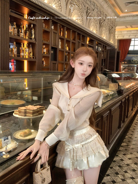 Model wearing a cream sheer blouse with a layered mini skirt in a café setting