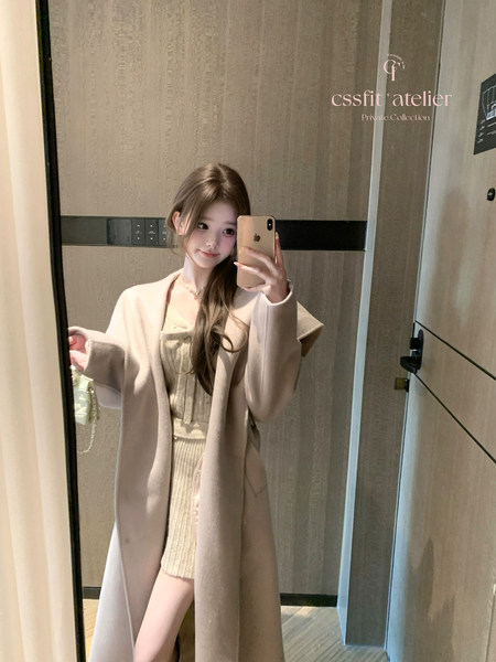 Woman wearing a beige coat over a knit dress in a mirror selfie