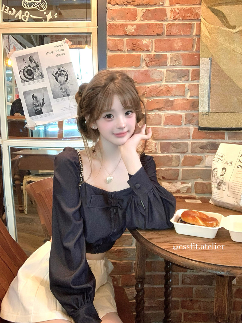 Model wearing a dark long-sleeve blouse with a cream skirt in a cafe setting