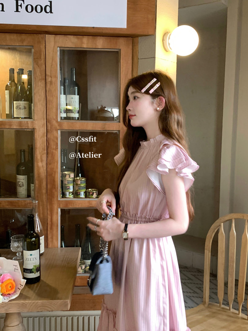Woman wearing a light pink pleated dress with flutter sleeves in a cafe setting