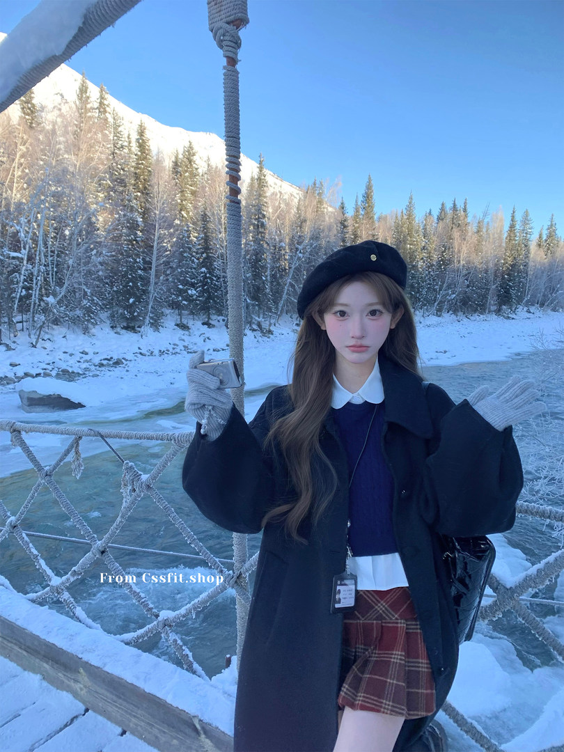 Female model wearing a black coat, beret, and plaid skirt in a snowy outdoor scene