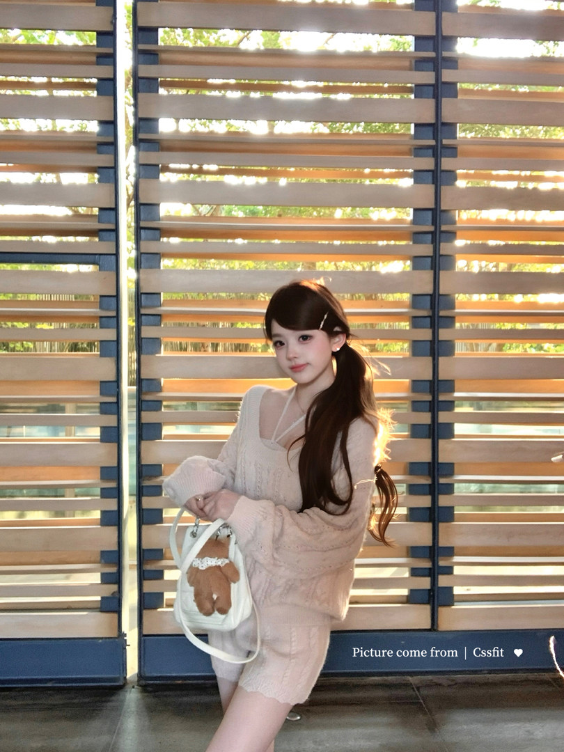 Woman wearing a light pink knit sweater and shorts set while holding a white handbag